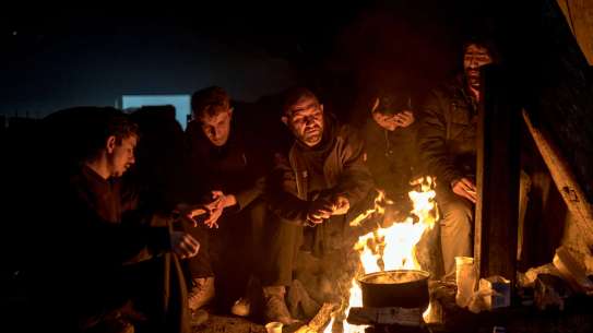 Five men sitting around a campfire in the dark.