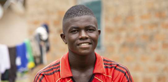 Imote sits in front of his house in Nigeria smiling