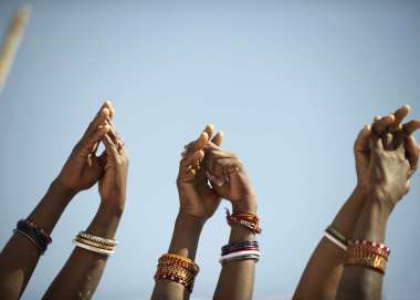 Image shows three pairs of arms reaching to the sky with hands clasped in pairs linking in a chain